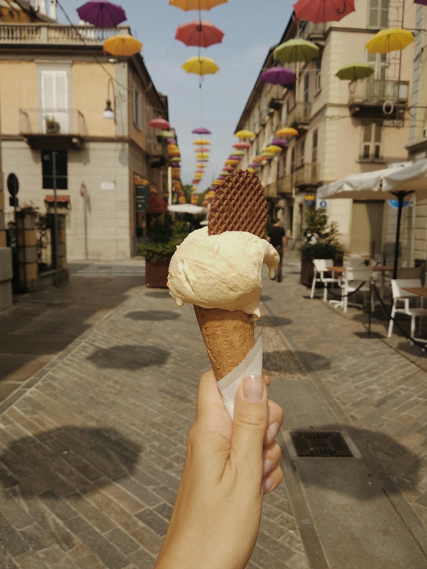 Hand holding an Italian gelato cone on a sun-drenched street