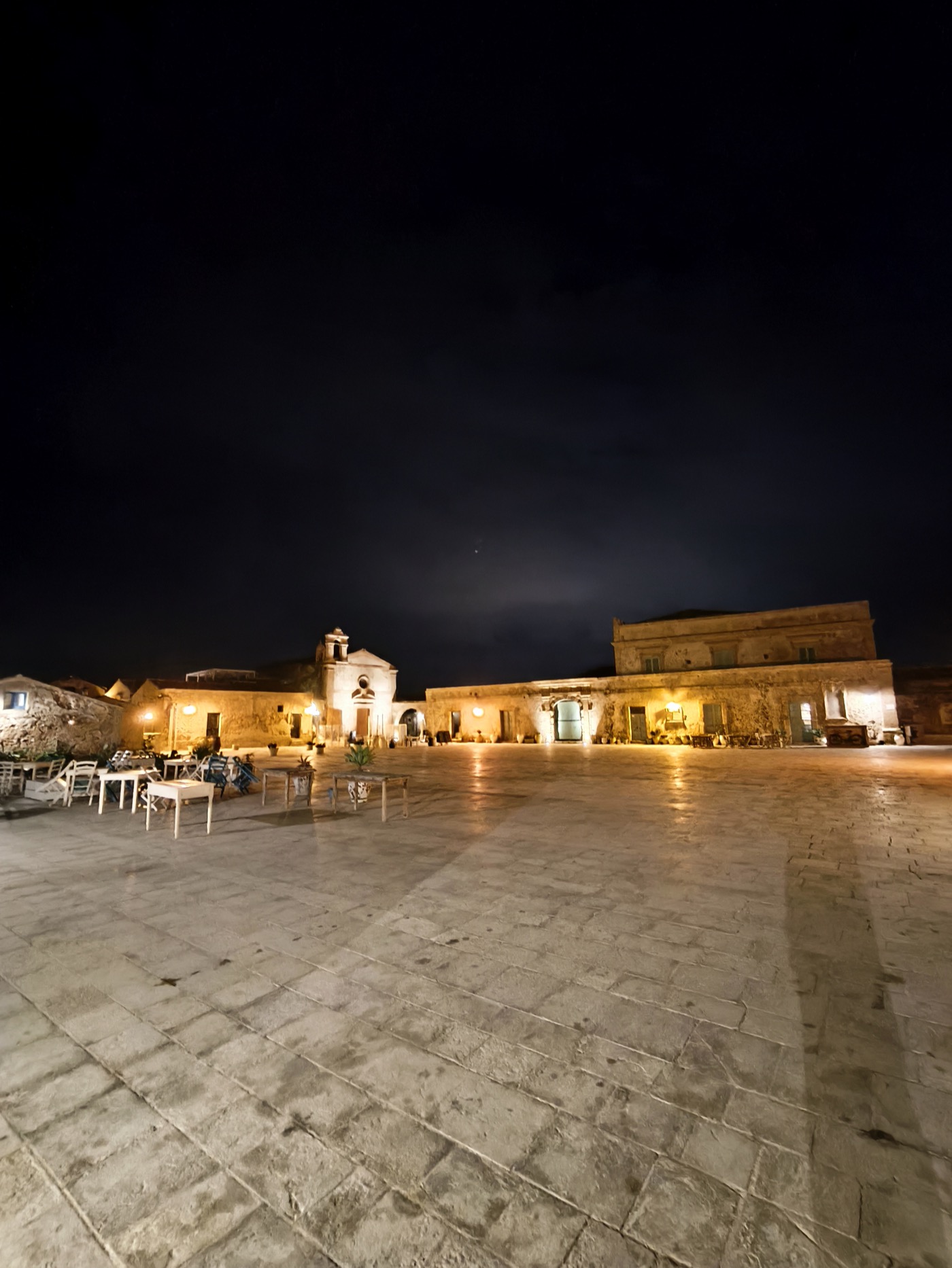Marzamemi piazza at night, stone buildings warmly lit with restaurant tables