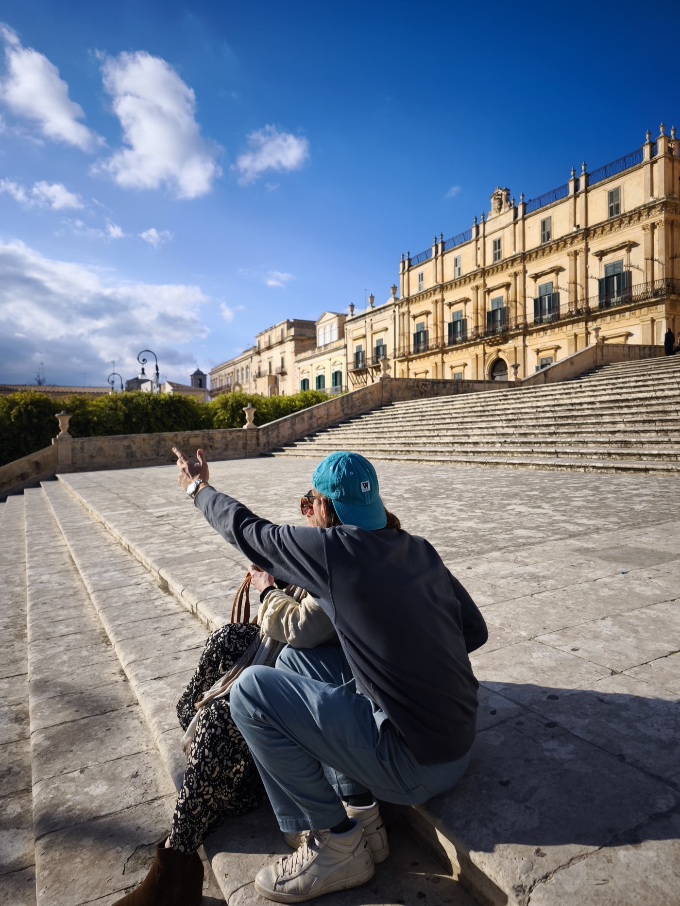 Visitors sitting on the wide stone staircase of a Baroque palazzo in Noto
